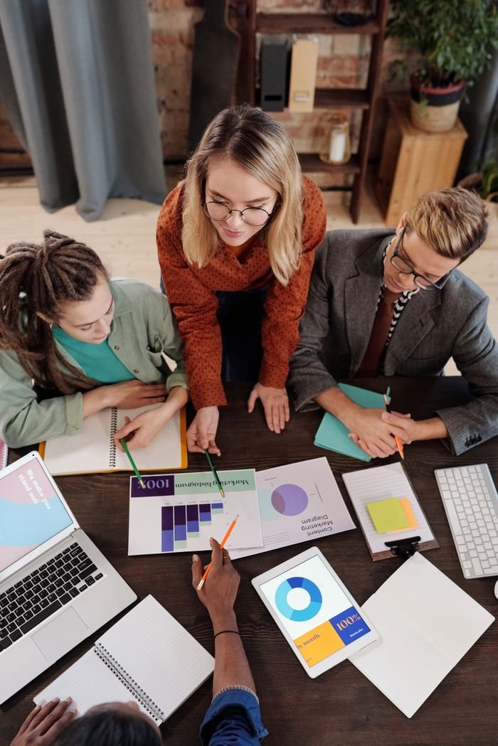 Top view of a diverse group discussing business reports and charts around a desk.